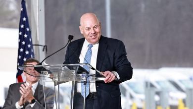 Postmaster General Louis DeJoy at a podium speaking to an audience.
