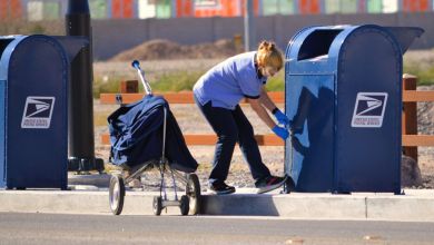 A female USPS worker bends to open a letter drop box and take the mail to the processing center.
