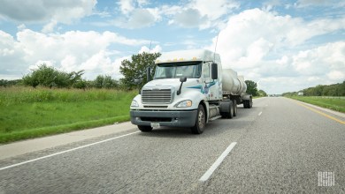 A white Dupre tractor pulling a tank trailer on a highway