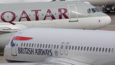 Close up side view of Qatar Airways and British Airways jets perpendicular to each other at an airport.