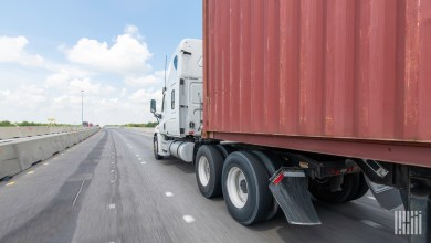 a white sleeper cab pulling an ocean container on a highway