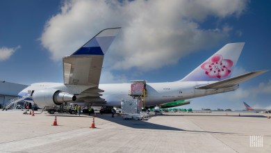 A large China Cargo Airlines 747-400 loading cargo at an airport. Pink flower design on the tail fin.
