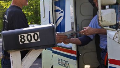 Close up a mailman in vehicle exchanging mail with a resident at mailbox.
