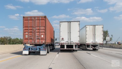 A rear view of one ocean container and two dry van trailers being pulled on a highway