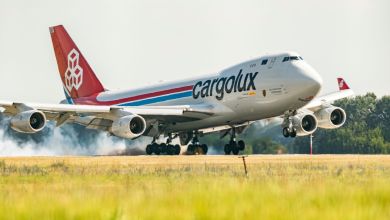 A red-tailed Cargolux jumbo jet touches down on a runway, with green grass in foreground.