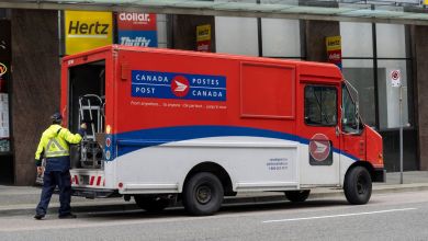 A Canada Post driver lifts a hand truck out of mail delivery vehicle on a city street.