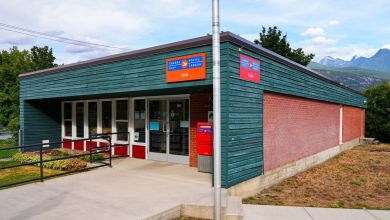 A rural Canada Post post office. Square building with mountains in the background.