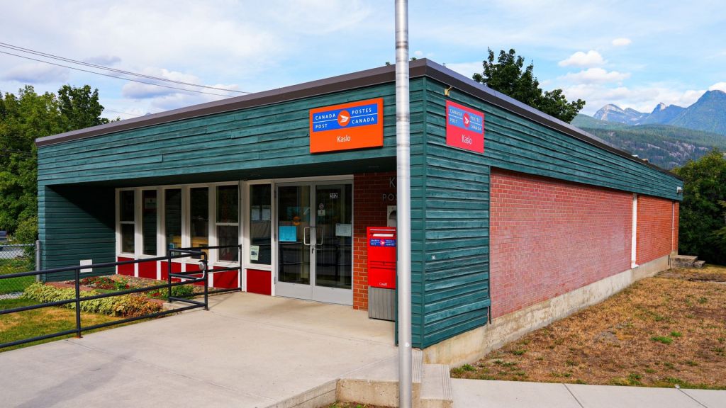 A rural Canada Post post office. Square building with mountains in the background.