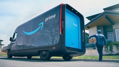 Two-tone blue Amazon Prime delivery van in front of a house, with driver delivering to doorstep.