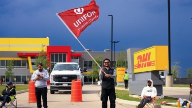 Workers picket a DHL facility waving a read Unifor flag.