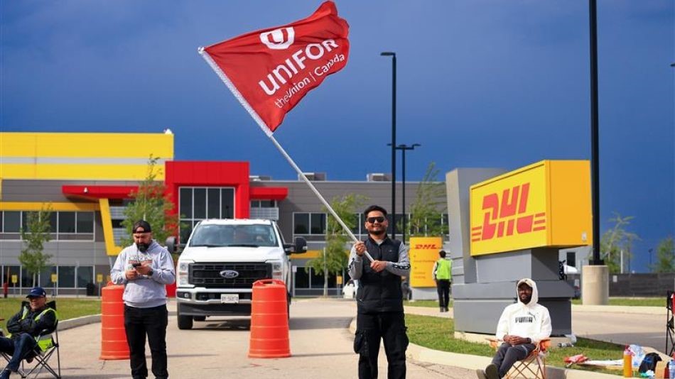 Workers picket a DHL facility waving a read Unifor flag.