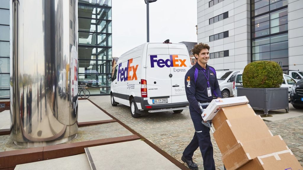 A FedEx driver pushes a handcart with packages after loading up from his van.