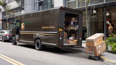 A brown UPS truck parked on a city street as driver unloads boxes.