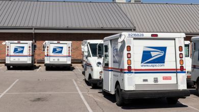 White U.S. Postal Service vans are parked at a local post office.
