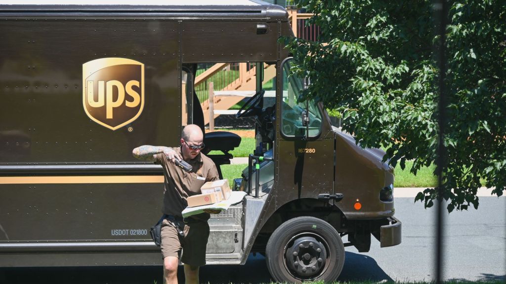 A UPS driver scans a package after exiting brown delivery truck.
