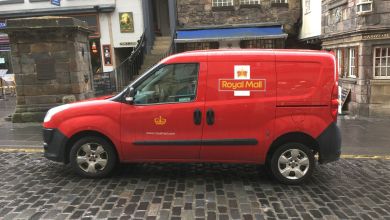 A red Royal Mail van parked on a cobblestone street.