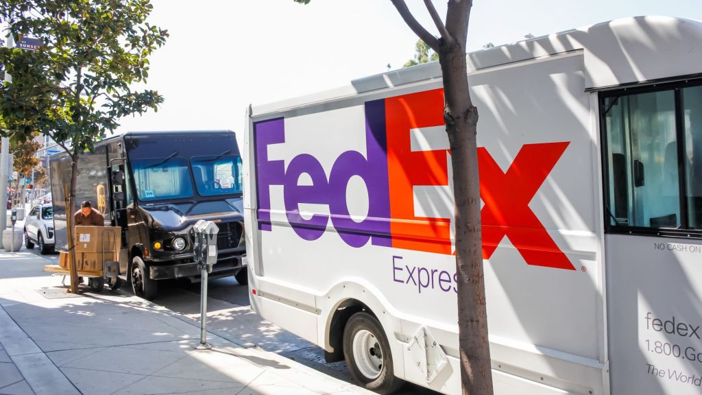 A brown UPS truck and white FedEx truck with blue and orange lettering parked along a curb.