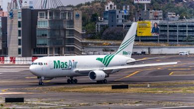 A MasAir cargo jet moves into position at the end of a runway with city buildings visible in the background.