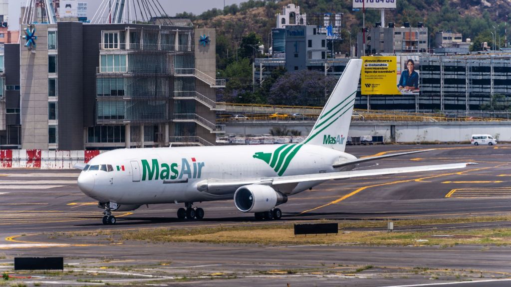 A MasAir cargo jet moves into position at the end of a runway with city buildings visible in the background.