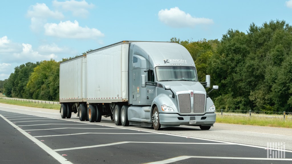 A silver Knight sleeper cab pulling two pup trailers on a highway