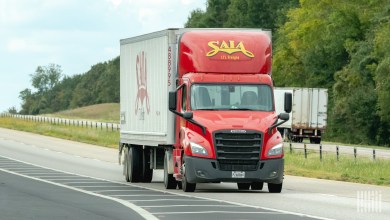 A red Saia daycab tractor pulling a white Saia trailer on a highway