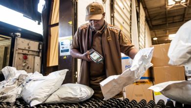 A man in a brown UPS uniform scans packages on a shelf.