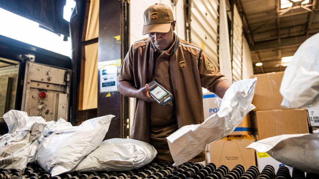 A man in a brown UPS uniform scans packages on a shelf.
