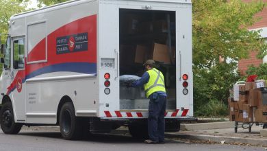 A mailman looking in the open rear door of a red-white-and-blue Canada Post van.