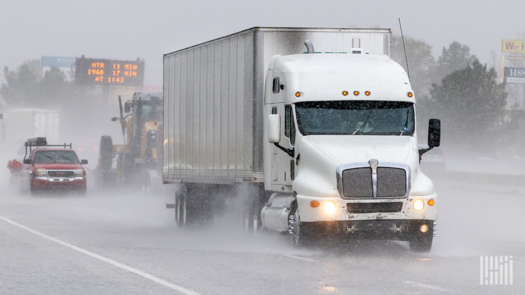 a lone white tractor pulling a silver dryvan trailer on a rainy highway