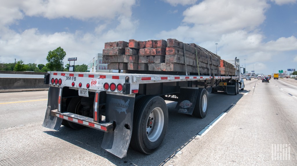 a flatbed trailer with center beams being pulled by a tractor on a highway