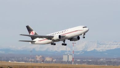 A blue-tailed Cargojet aircraft takes off from a runway with mountains in the background.