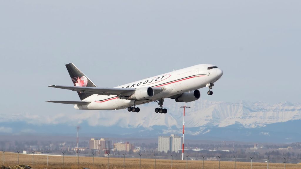 A blue-tailed Cargojet aircraft takes off from a runway with mountains in the background.
