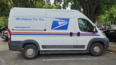 A modern USPS delivery van sits in a parking lot.