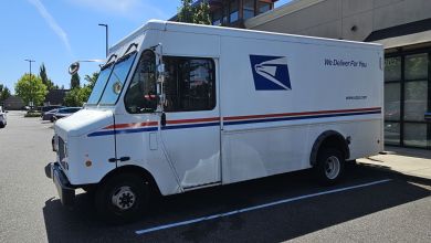 Close up side view of a USPS van parked in a strip mall.