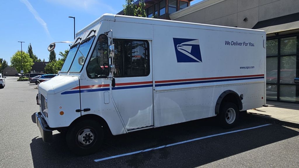 Close up side view of a USPS van parked in a strip mall.