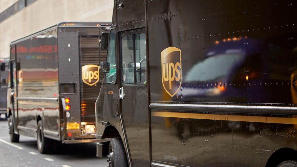 A closeup angled view of two brown UPS vans along a street curb.