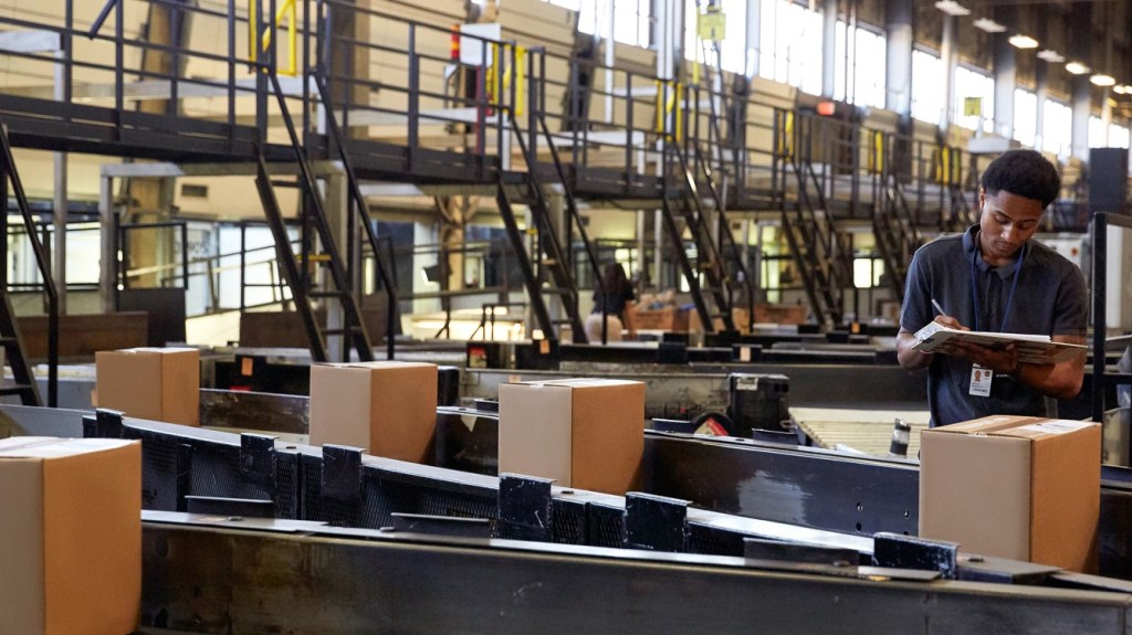 A UPS warehouse worker checks packages on a conveyor belt.