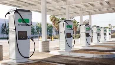 Greenlane EV charging stations under a covered area with palm trees in the background, featuring multiple chargers with cables, designed for electric trucks at the Colton facility.