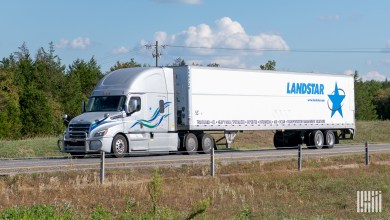 a silver sleeper cab pulling a white Landstar trailer on a highway