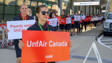A flight attendant on a picket line holds an orange sign "UnfAir Canada"