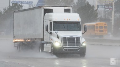 a white sleeper cab pulling a trailer on a rainy highway