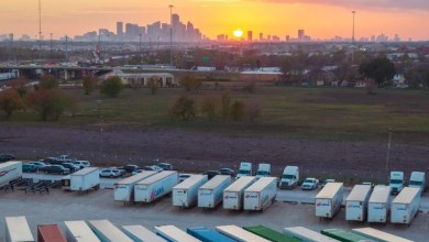 Aerial view of a truck terminal yard with parked semi-trailers and trucks at sunset, overlooking a city skyline, showcasing efficient freight operations enhanced by Outpost's AI-powered gate automation platform.