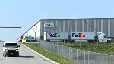 A FedEx distribution center with FedEx Ground trucks and small delivery vans driving by and parked .