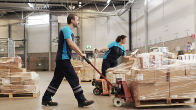 A warehouse worker in blue uniform moves a pallet of packages.