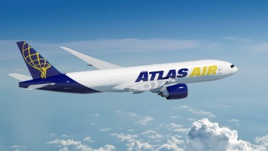 A blue-tailed Atlas Air cargo jet with gold accents flies above the clouds.