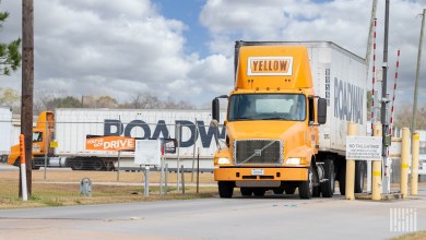 A Yellow daycab pulling a Roadway trailer through a terminal gate