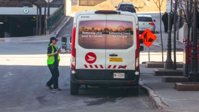 A Canada Post mail carrier opens door of delivery van on a city street, as viewed from behind vehicle.
