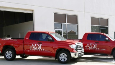 Red pickup trucks with ADL Delivery name painted on the side, parked in front of a warehouse garage.