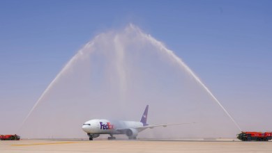A FedEx plane receives a water cannon salute at an airport, with water sprayed above it.
