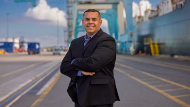 Image shows a man standing dockside in front of a container crane.